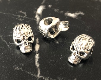 May include: Three silver skull charms with detailed designs. The skulls have a textured surface and are a popular choice for jewelry making.