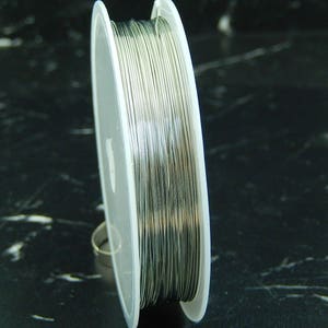 Può includere: Un rocchetto di filo color argento su un rocchetto di plastica bianca. Il filo è avvolto strettamente attorno al rocchetto.