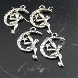 Peut inclure: Quatre pendentifs de charme en argent en forme de croissant de lune avec une fée assise dessus. Chaque charme a une petite étoile sur la lune.