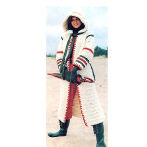 May include: A long, hooded crochet coat in cream with red and green accents. The coat features a hood, long sleeves, and a full-length design. The trim and edges are detailed with red and green stripes. The person is wearing green boots and gloves.