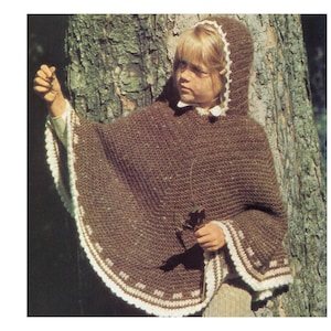 Könnte beinhalten: Ein braunes Häkelponcho mit weißen Verzierungen. Das Poncho hat eine Kapuze und wird von einer jungen Person getragen, die vor einem Baum steht.