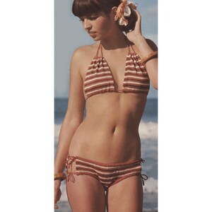 May include: A two-piece bikini set with a halter top and low-rise bottoms. The bikini is made of a striped fabric in shades of brown and white. The top and bottoms have a drawstring detail. The background shows the ocean.