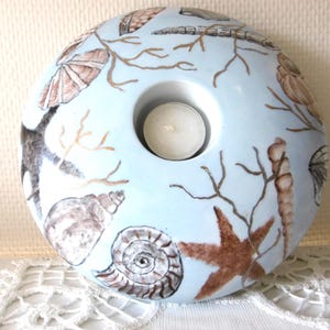 Peut inclure: Un bougeoir en céramique bleu clair avec une ouverture centrale pour une bougie chauffe-plat. Le bougeoir est décoré de coquillages, d'étoiles de mer et de coraux bruns et beiges. Le bougeoir mesure environ 10 cm de diamètre.