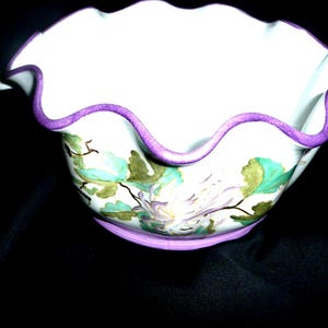 Peut inclure: Un bol en céramique blanche avec un bord festonné et une bordure violette. Le bol est décoré d'un motif floral dans des tons de vert, blanc et violet.