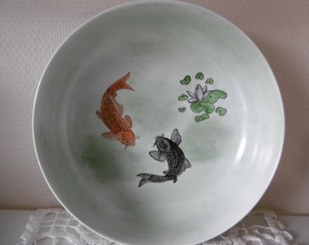 Hand-painted porcelain bowl decorated with two fish and a lotus on a Japanese-inspired green background