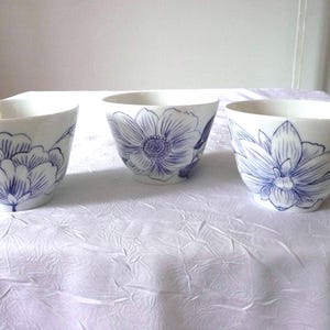 Peut inclure: Trois bols en céramique blanche avec des motifs floraux bleus. Les bols ont des motifs floraux différents, notamment des pivoines, des anémones et des nénuphars.