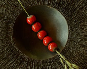 May include: A string of five red ceramic beads on a thin stem, resting in a dark brown bowl with a textured surface.