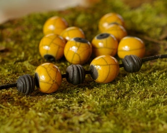 May include: A necklace made of yellow and black ceramic beads. The beads are round and have a crackled finish. The necklace is lying on a bed of green moss.