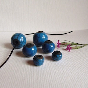 Peut inclure: Un ensemble de six perles en céramique bleues et noires avec un glaçage craquelé. Les perles sont enfilées sur un cordon noir.