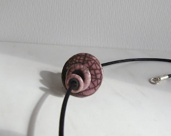 May include: A pink ceramic bead with black crackle glaze, strung on a black cord necklace.