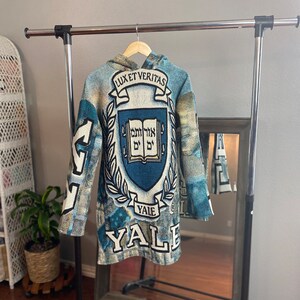 May include: A blue and white tapestry hoodie with the Yale University crest and the words "Lux et Veritas" and "Yale" on the front.