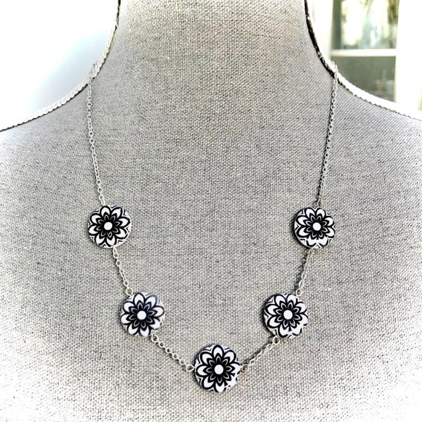 Collier fleuri composé de perles plates en nacre blanc avec motifs fleurs noires avec chaine en métal argenté pour femme