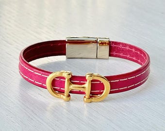 Fuchsia roze leren damesarmband met witte stiksels, een paardenbit-bedel en een magneetsluiting van goudkleurig metaal.