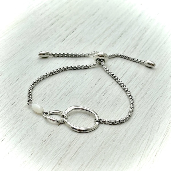 Bracelet en métal argenté réglable par lien coulissant avec connecteur anneaux entrelacés argent brillant et perle olive en nacre pour femme