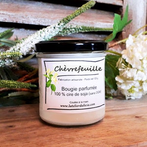 Pu&ograve; includere: Una candela di vetro in un barattolo con un'etichetta bianca che recita "Ch&egrave;vrefeuille" e "Bougie parfum&eacute;e 100% cire de soja (sans OGM)". L'etichetta include anche il testo "Fabrication artisanale - Poids net 125g" e "Coul&eacute;e &agrave; la main" e il sito web "www.latelierdalicia.com".