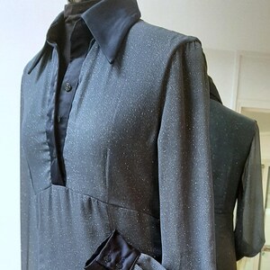 Peut inclure: Robe gris foncé avec un léger effet scintillant. Elle présente des manches longues avec des poignets noirs, un col noir et une bordure noire assortie autour de l'encolure. La robe a une jupe évasée.