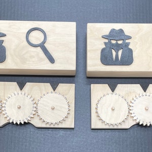 May include: Two wooden boxes with a spy and magnifying glass design on the top. Each box has three wooden gears with letters on them.