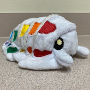 May include: A white plush toy shaped like a pill bug with a rainbow pattern on its back. The toy has black eyes and a yellow highlight.