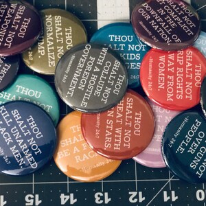 May include: A collection of colorful round buttons with white text. The buttons feature various phrases, including "Thou Shalt Not" followed by different directives. The buttons are in shades of blue, red, yellow, and purple.