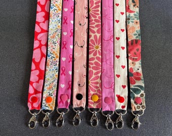 Puede incluir: Ocho cordones de tela dispuestos verticalmente, cada uno con patrones distintos que incluyen corazones rojos, estampados florales, cintas rosas de concienciación sobre el cáncer de mama, arte lineal abstracto, margaritas rosas y corazones.