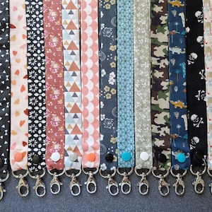 Peut inclure: Une collection de lanières à motifs avec divers designs, notamment des formes géométriques, des cœurs, des motifs floraux et des dinosaures. Chaque lanière est dotée d'un fermoir en métal et d'une fermeture à bouton. Les lanières sont de couleurs variées, dont le noir, le blanc, le rose et le bleu.