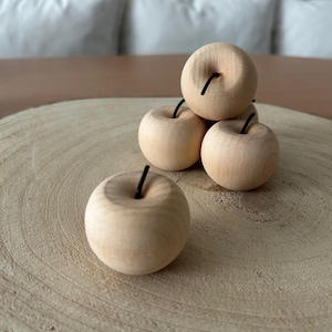Op de afbeelding: Een verzameling van vijf houten appelsculpturen met een natuurlijke houten afwerking. Elke appel heeft een kleine, donkere steel. De appels zijn gerangschikt op een lichtgekleurd, cirkelvormig houten oppervlak, wat een rustieke en natuurlijke uitstraling creëert.
