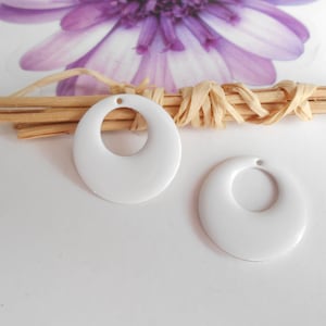 May include: Two white plastic oval-shaped embellishments with a hole in the centre. The embellishments are on a white surface.