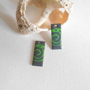 May include: Two gray rectangular metal charms with a green spiral design.