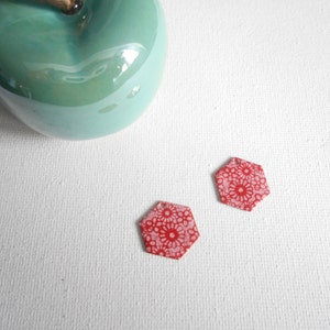 May include: Two red hexagonal ceramic earrings with a white floral pattern.