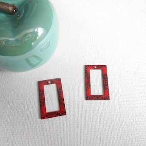 May include: Two red rectangular metal charms with a black patterned design and a hole at the top.