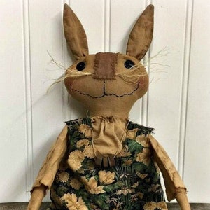 Puede incluir: Un conejito de trapo hecho a mano con un vestido floral verde y amarillo. El conejito tiene una nariz marrón y ojos negros.
