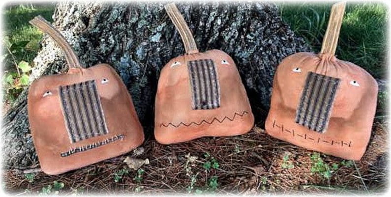 May include: Three brown fabric pumpkins with stitched-on eyes and mouths. Each pumpkin has a striped fabric panel for a nose.
