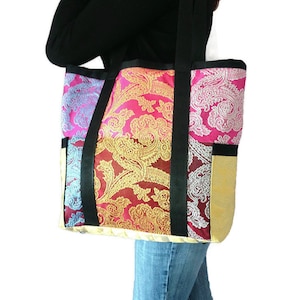 Könnte beinhalten: Eine große, farbenfrohe Tragetasche mit Patchwork-Design. Die Tasche besteht aus verschiedenen Stoffen mit Paisley-Mustern in den Farben Pink, Blau, Gold und Rot. Die Tasche hat schwarze Trageriemen und einen goldenen Besatz.