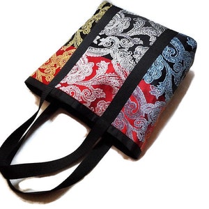 Peut inclure: Un sac fourre-tout coloré avec un motif cachemire en or, rouge, noir et bleu. Le sac a des poignées et des bordures noires. Le sac est fait d'un tissu à motifs.