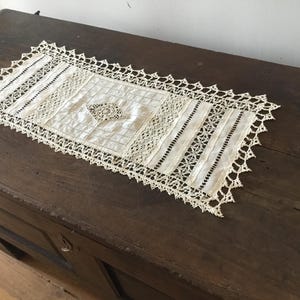 Peut inclure: Un chemin de table en crochet blanc avec un motif de dentelle délicat. Le chemin de table est posé sur une surface en bois foncé.