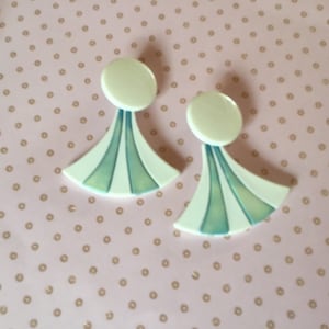 Peut inclure: Une paire de boucles d'oreilles blanches imposantes avec un motif géométrique bleu et blanc. Les boucles d'oreilles ont un dessus rond et un bas en forme d'éventail.