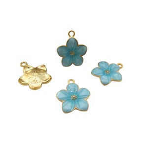 Może przedstawiać: Cztery zawieszki w kształcie kwiatów. Trzy są jasnoniebieskie ze złotymi krawędziami i środkami. Jedna jest w kolorze złotym. Każda zawieszka ma małą pętlę do mocowania do biżuterii lub innych rękodzieł. Zawieszki są na białym tle.