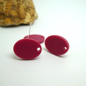Pode incluir: Dois brincos ovais com fecho de pino. Os brincos são de cor vermelho-bordo escuro.