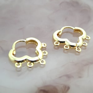 Op de afbeelding: Een paar gouden oorringen in de vorm van een klavertje vier met vier springringen die aan elke oorring hangen.