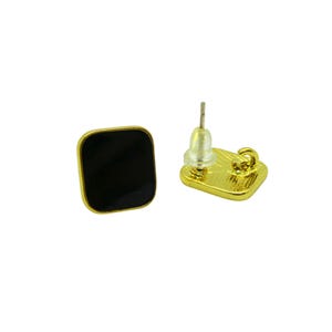 Peut inclure: Une paire de boucles d'oreilles carrées avec un centre en émail noir et un bord doré. Une boucle d'oreille est présentée face visible, l'autre montre la tige et le fermoir.