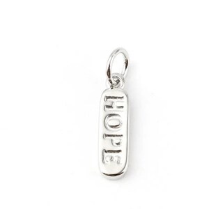 Può includere: Ciondolo in argento con la parola "HOPE" incisa. Il ciondolo ha la forma di un piccolo rettangolo con bordi arrotondati.