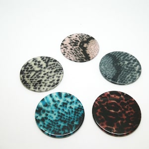 Può includere: Cinque pezzi rotondi e piatti decorativi con diversi disegni di stampa animalier. I disegni includono bianco e nero, rosa e nero, blu e nero e marrone e nero.