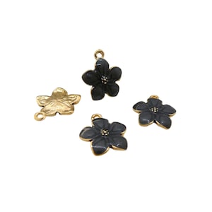Może przedstawiać: Cztery zawieszki w kształcie kwiatów. Jedna jest w kolorze złotym, pozostałe trzy są ciemnoszare ze złotymi krawędziami. Każda zawieszka ma małą pętlę do mocowania do biżuterii lub innych prac rzemieślniczych.