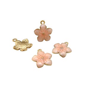Może przedstawiać: Cztery zawieszki w kształcie kwiatów. Trzy są jasnoróżowe ze złotymi krawędziami i małą pętelką u góry. Jedna jest złota z teksturowaną powierzchnią. Zawieszki te nadają się do tworzenia biżuterii lub projektów rzemieślniczych.