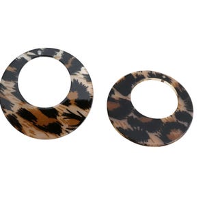 Peut inclure: Deux boucles d'oreilles circulaires avec un motif léopard. Les boucles d'oreilles ont une finition brillante avec des taches noires, marron et beige. Les boucles d'oreilles sont de tailles différentes.