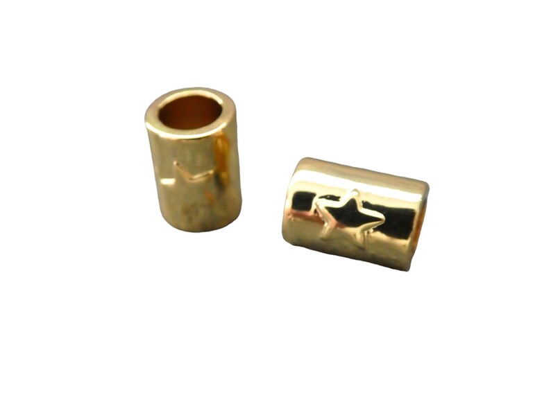 May include: Two gold-colored metal bead spacers with a star design. The spacers are cylindrical in shape and have a smooth, shiny finish.