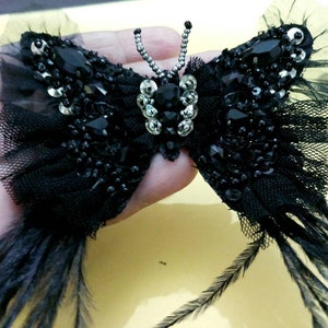 May include: Black butterfly-shaped embellishment with black feathers, sequins, and rhinestones.
