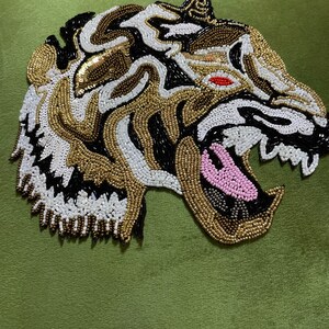 May include: A green velvet pillow with a beaded tiger design. The tiger is made of gold, black, white, and pink beads.