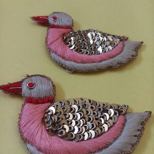 May include: Two embroidered pink and gray bird appliques with gold sequins. The birds have red beaks and eyes.