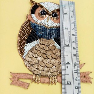 Op de afbeelding: Een geborduurde uil applique met een roze lint en gouden accenten. De uil is ongeveer 12,7 cm hoog.